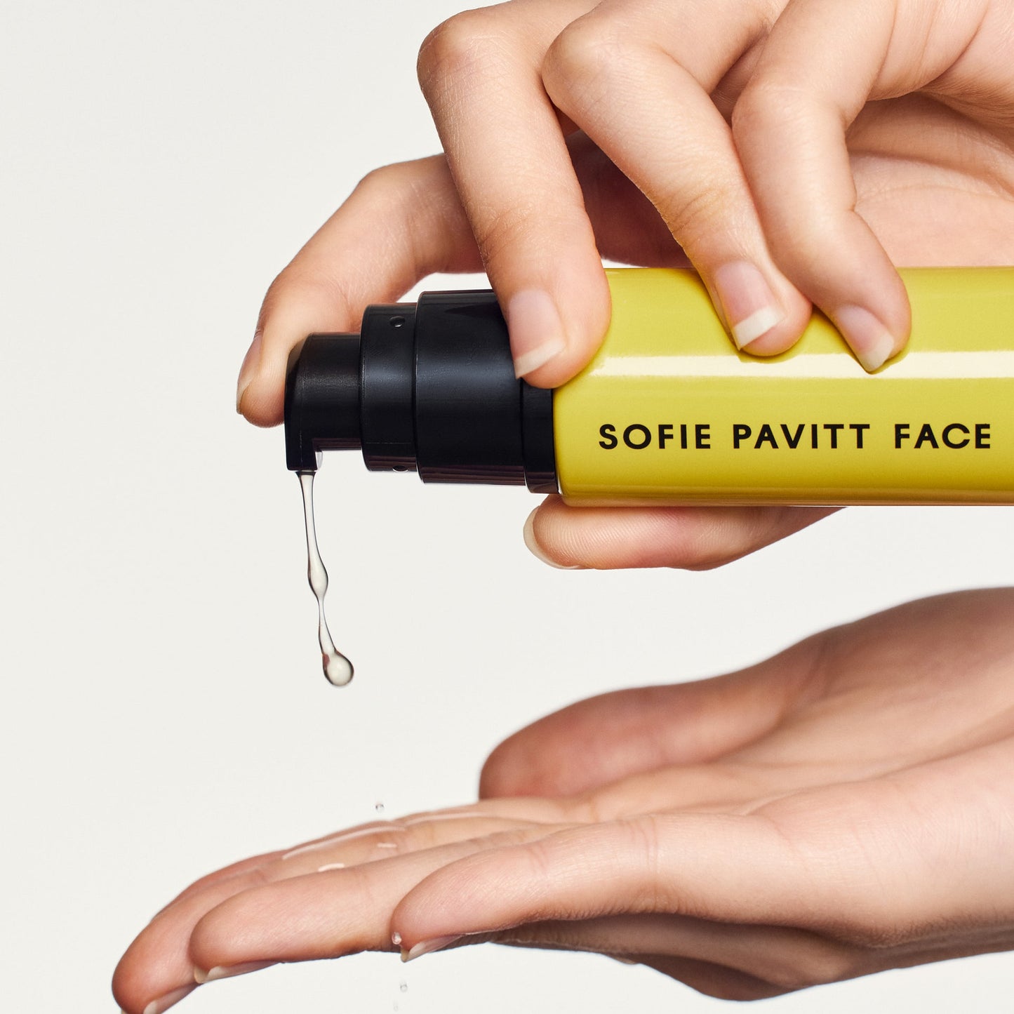 Hand holding a yellow bottle labeled 'SOFIE PAVITT FACE' with droplets on a light gray background