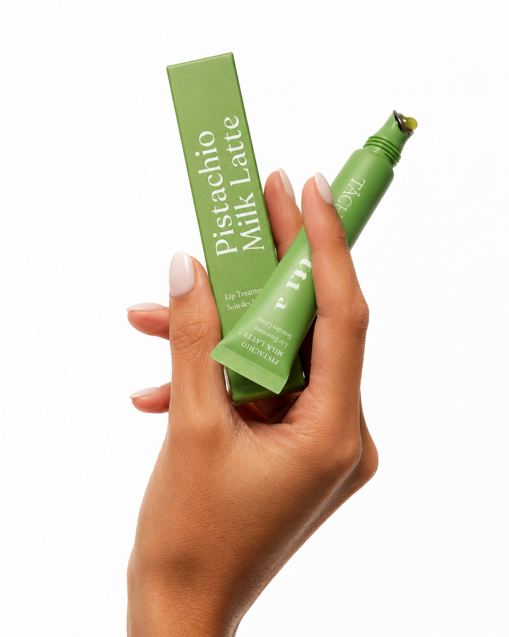 A hand holding a green tube of Nutra Botanica Pistachio Milk Latte Calm Skin Balm next to its matching green box, set against a solid white background.