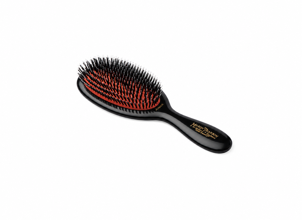 A black oval hairbrush with red and black bristles and gold text on the handle, shown on a plain white background.